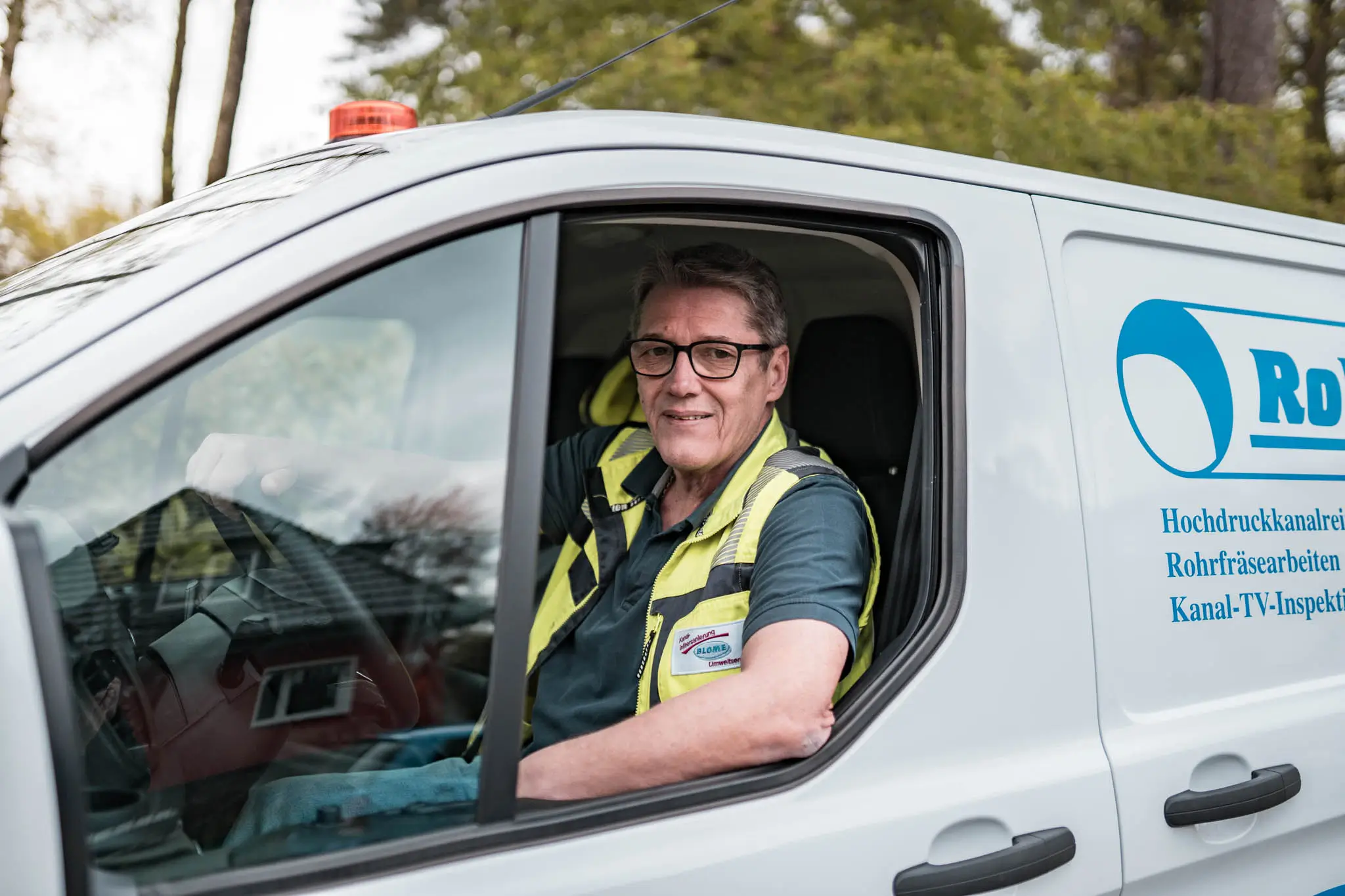 Fachmann für Rohrreinigung Benrath lächelt aus einem Firmenwagen.